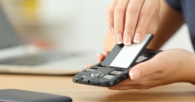 Рука извлекает съёмную батарею из смартфона