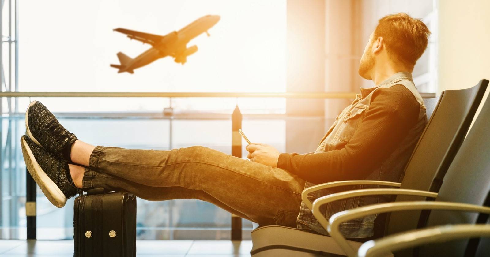 Мужчина сидит в аэропорту и смотрит на взлетающий самолёт