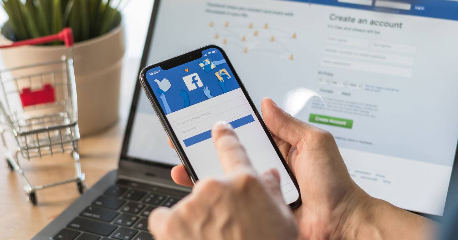 Мобильное приложение Facebook на смартфоне на фоне ноутбука с сайтом Facebook