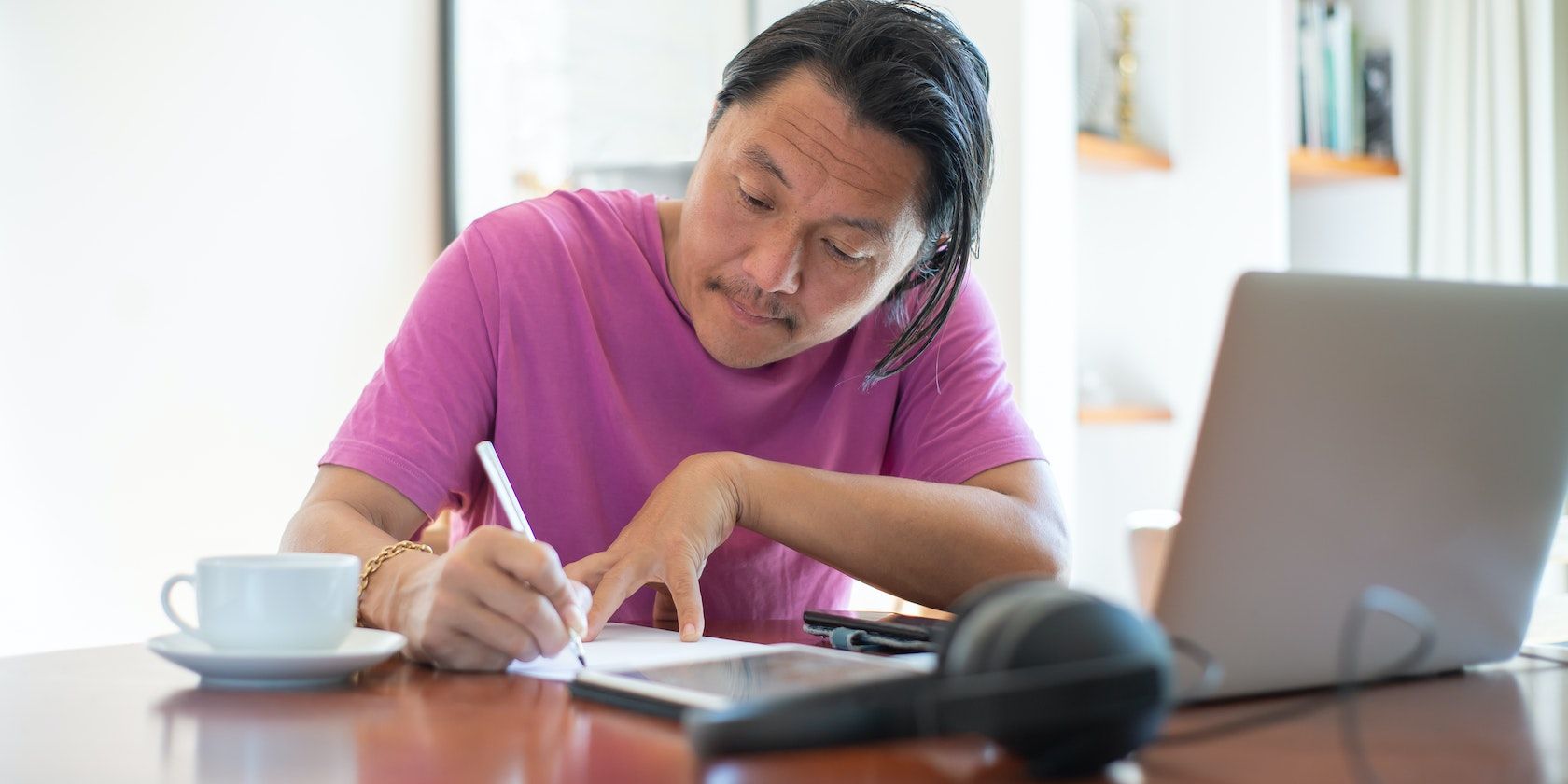 Мужчина в розовой рубашке пишет за столом