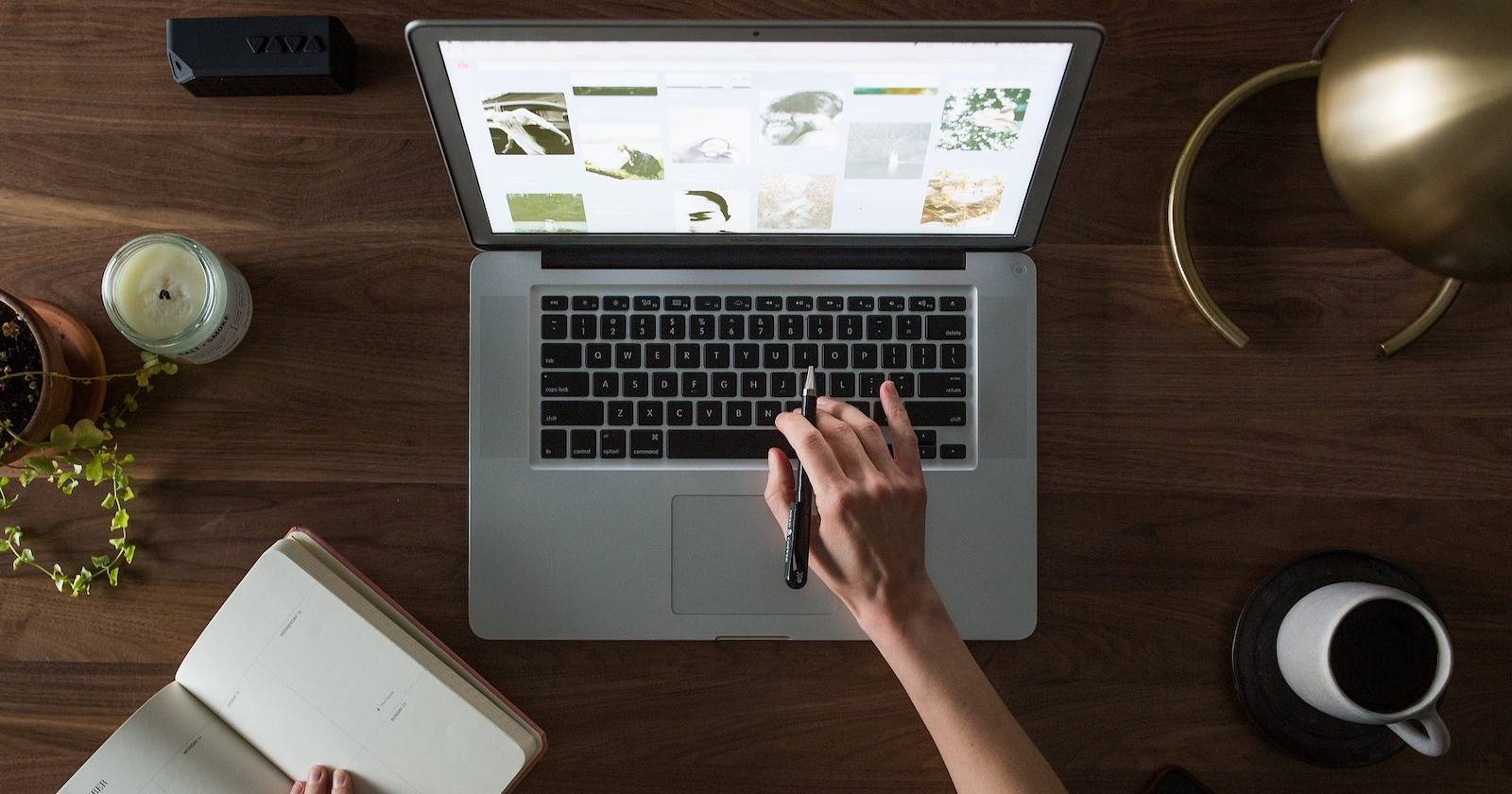 женские руки печатают на ноутбуке, стол с чашкой кофе, блокнотом, свечой и лампой