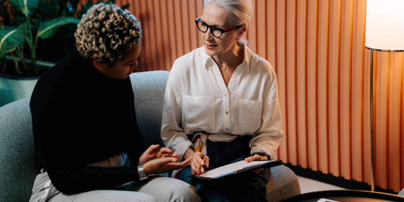 Две женщины на сером диване разговаривают.