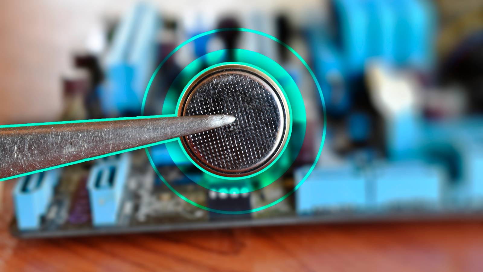 A tweezer holding a CMOS battery with a motherboard in the background.