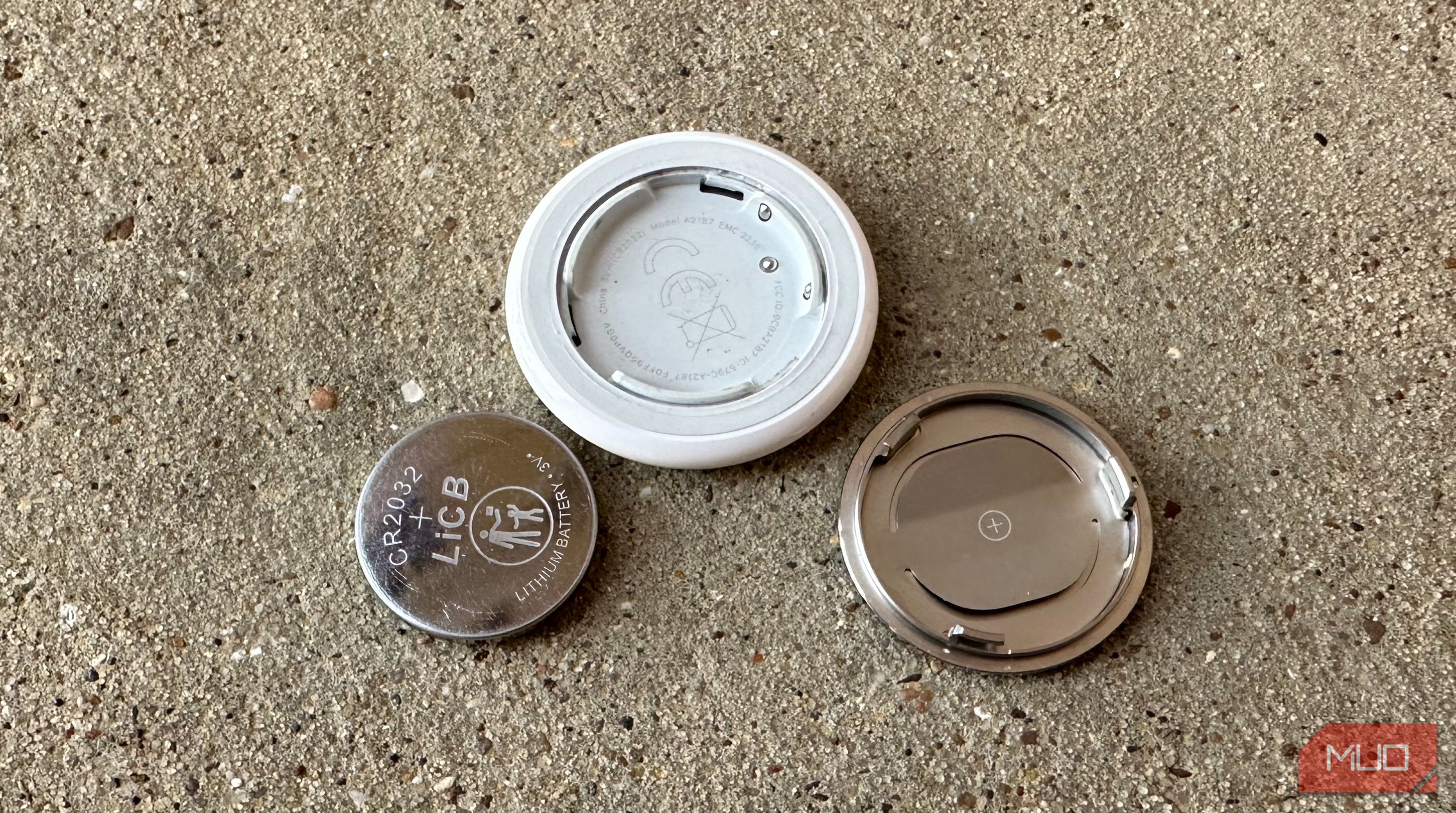Корпус AirTag и батарейка CR2032 на грубой поверхности