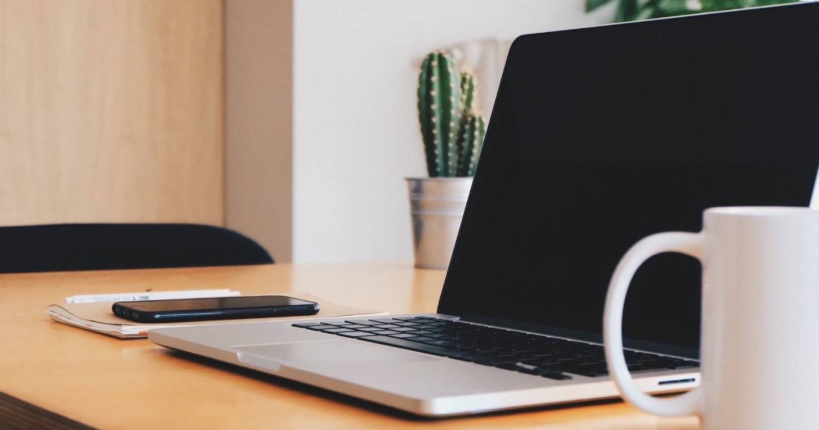 Компьютер, кружка с кофе, телефон и декоративное растение на рабочем столе