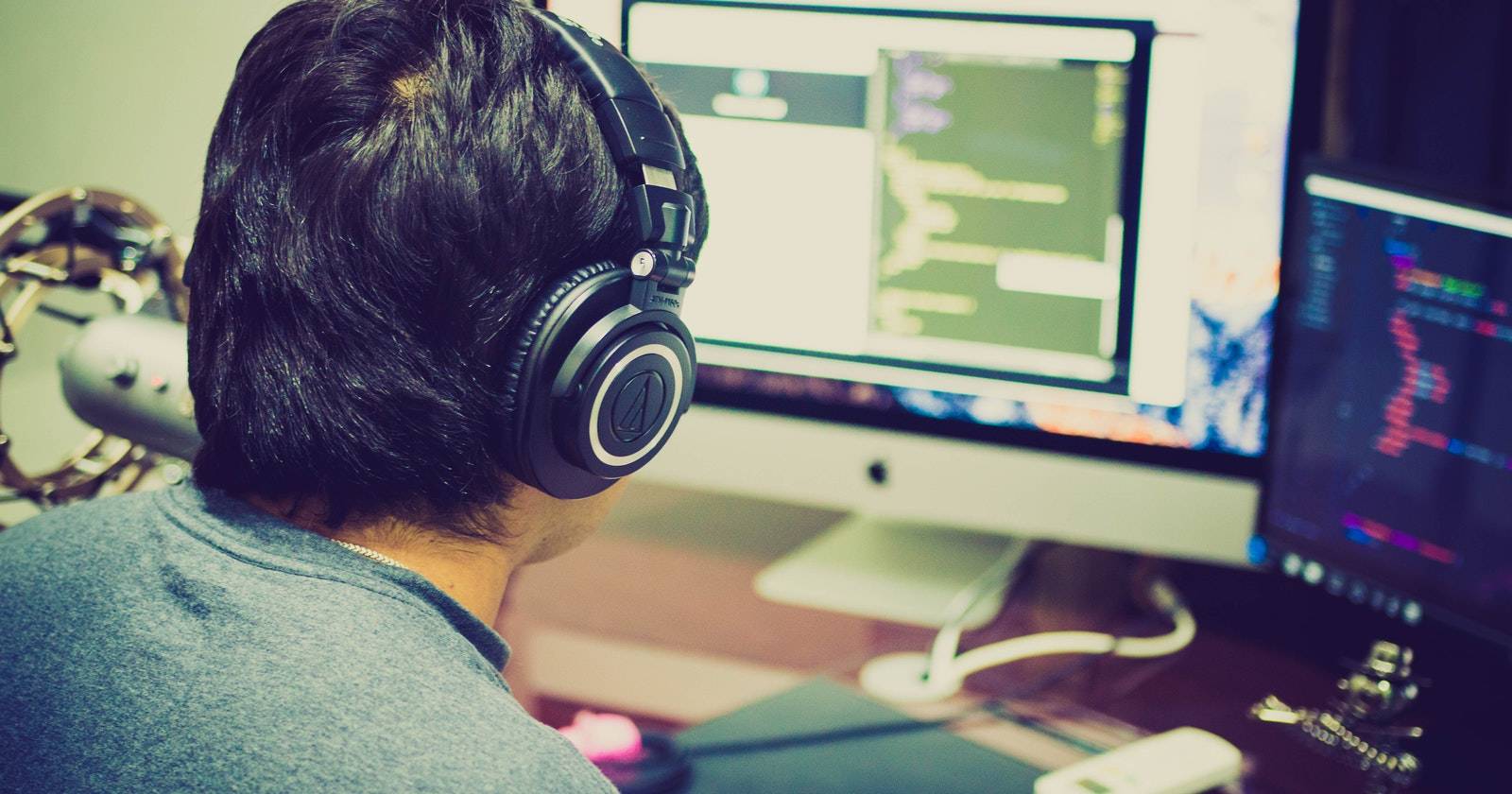 Вид сзади человека в наушниках перед двумя размытыми экранами