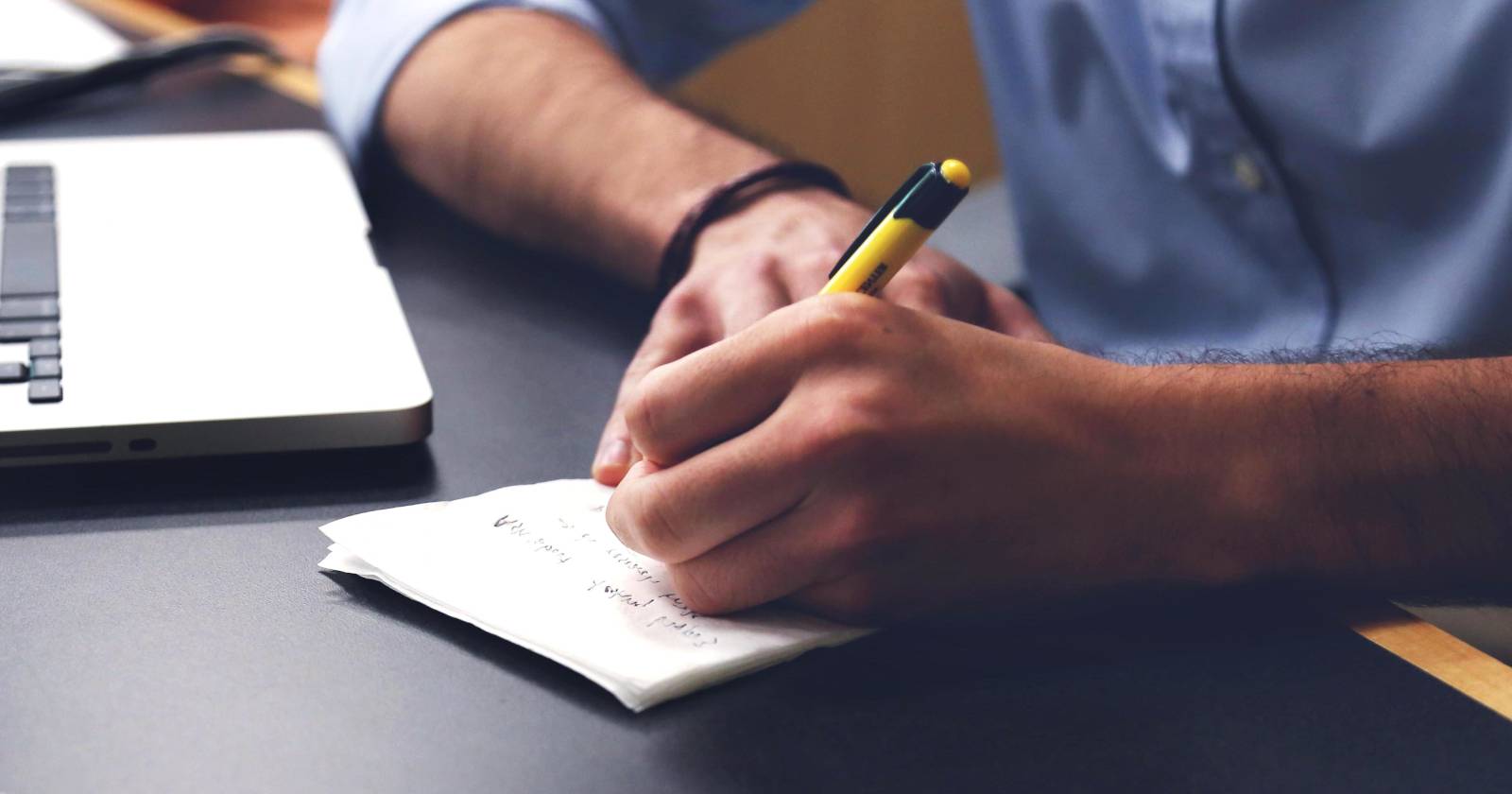 Человек делает заметки рядом с ноутбуком
