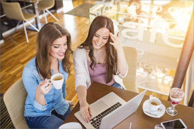 Two women working at one MacBook laptop in a cafe