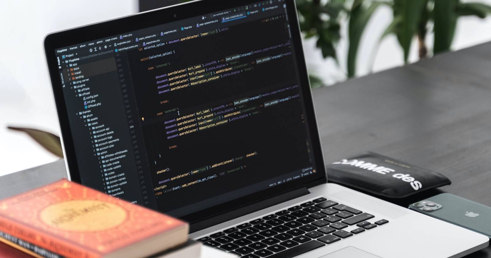 Ноутбук на столе рядом с книгами, на экране редактор кода с тёмной темой.