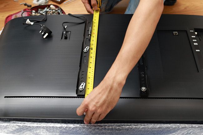 Человек измеряет высоту корпуса телевизора рулеткой