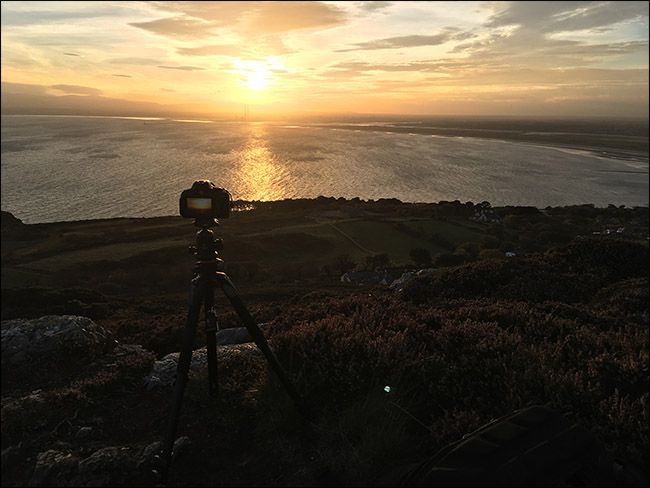 Фотограф устанавливает штатив на берегу озера перед рассветом