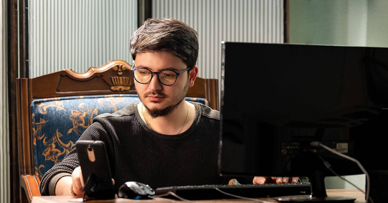 Мужчина за рабочим столом с телефоном и монитором, просматривающий сайты в интернете