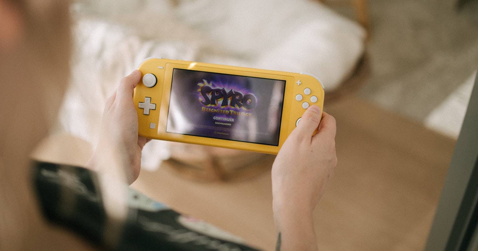 Фотография человека, держащего жёлтую консоль Nintendo Switch Lite с изображением игры Spyro Reignited Trilogy на экране