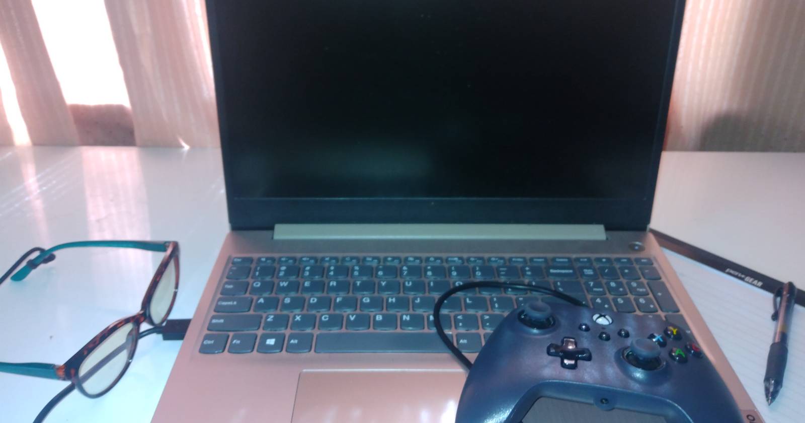 blue-light glasses, controller, notepad, and laptop on a desk