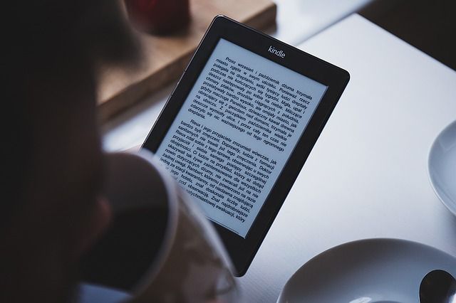 Человек читает Kindle на диване рядом с чашкой чая