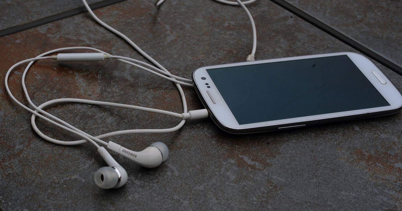 Фоновое изображение: рука держит смартфон с наушниками