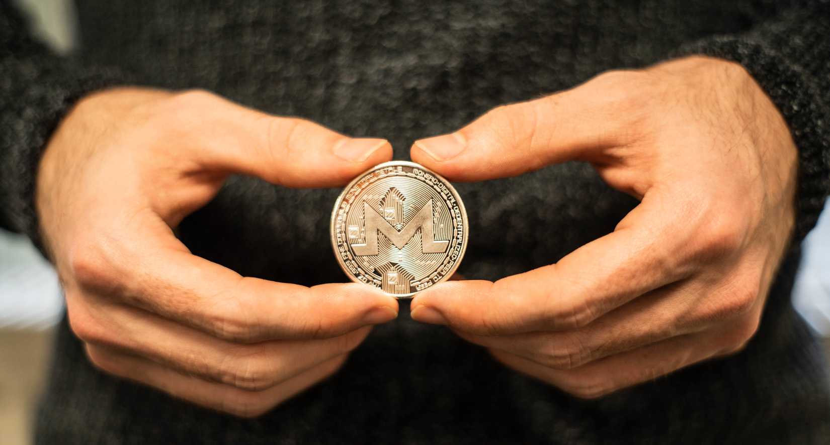 Человек держит монету Monero в руках