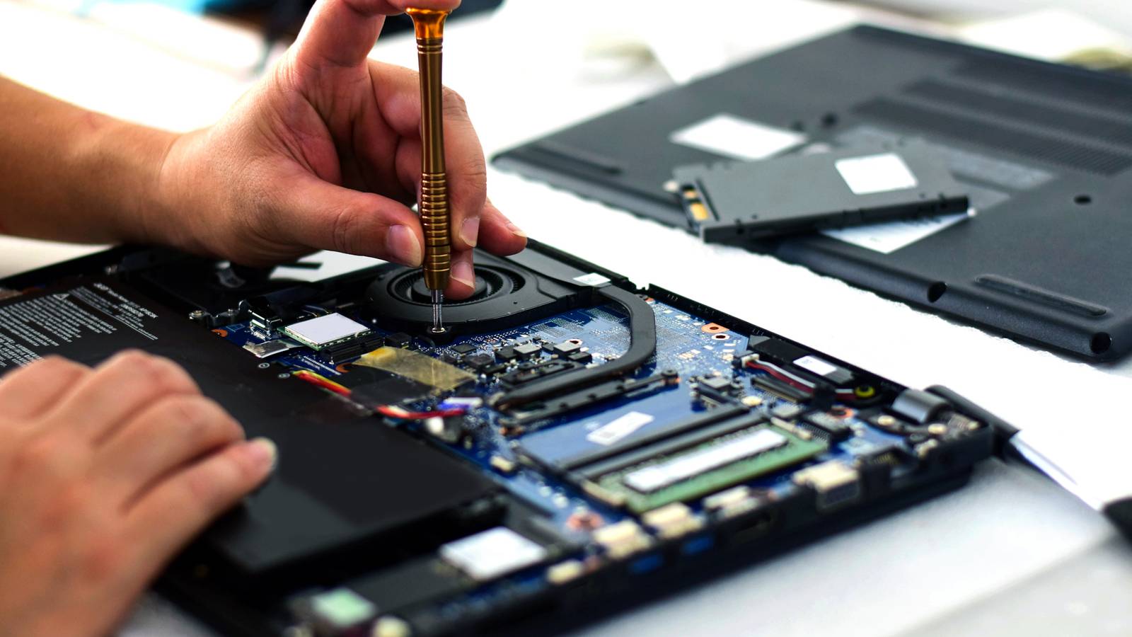 человек ремонтирует материнскую плату ноутбука отверткой