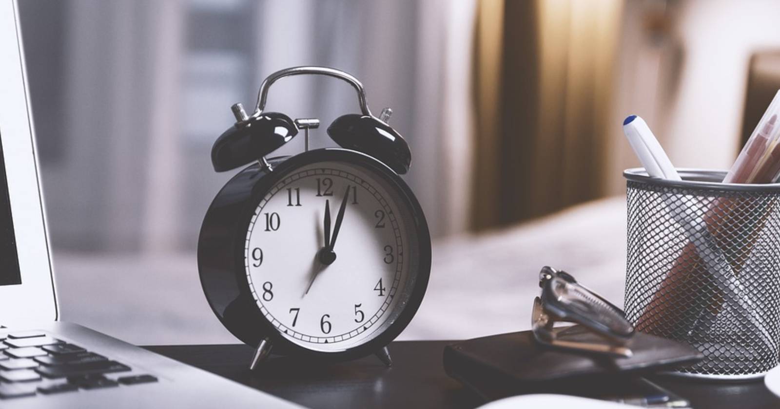Будильник рядом с ноутбуком и подставкой для ручек