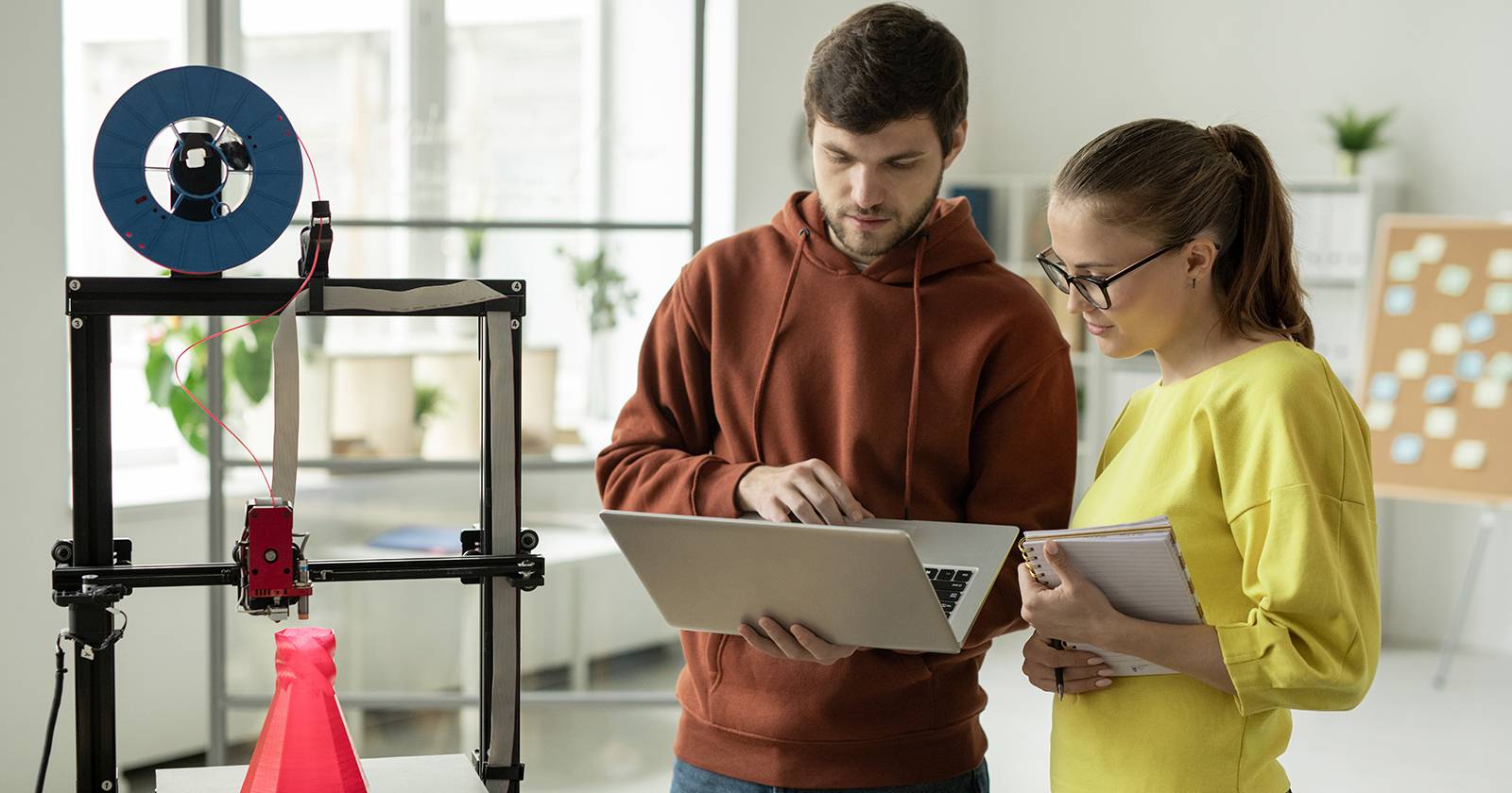 Два дизайнера по 3D-печати работают за ноутбуком рядом с 3D-принтером