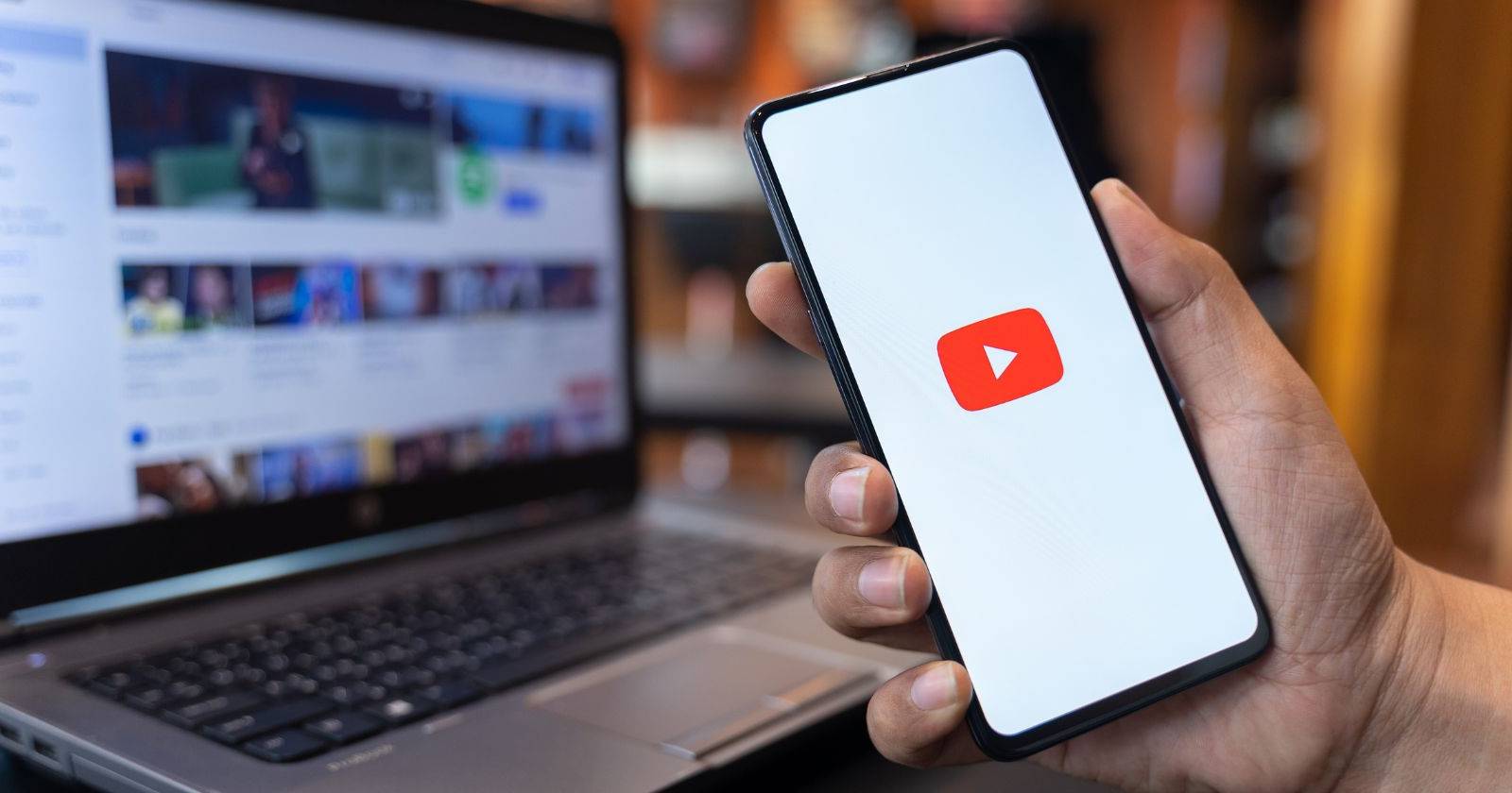 Человек держит телефон с приложением YouTube на экране, на фоне виден сайт YouTube