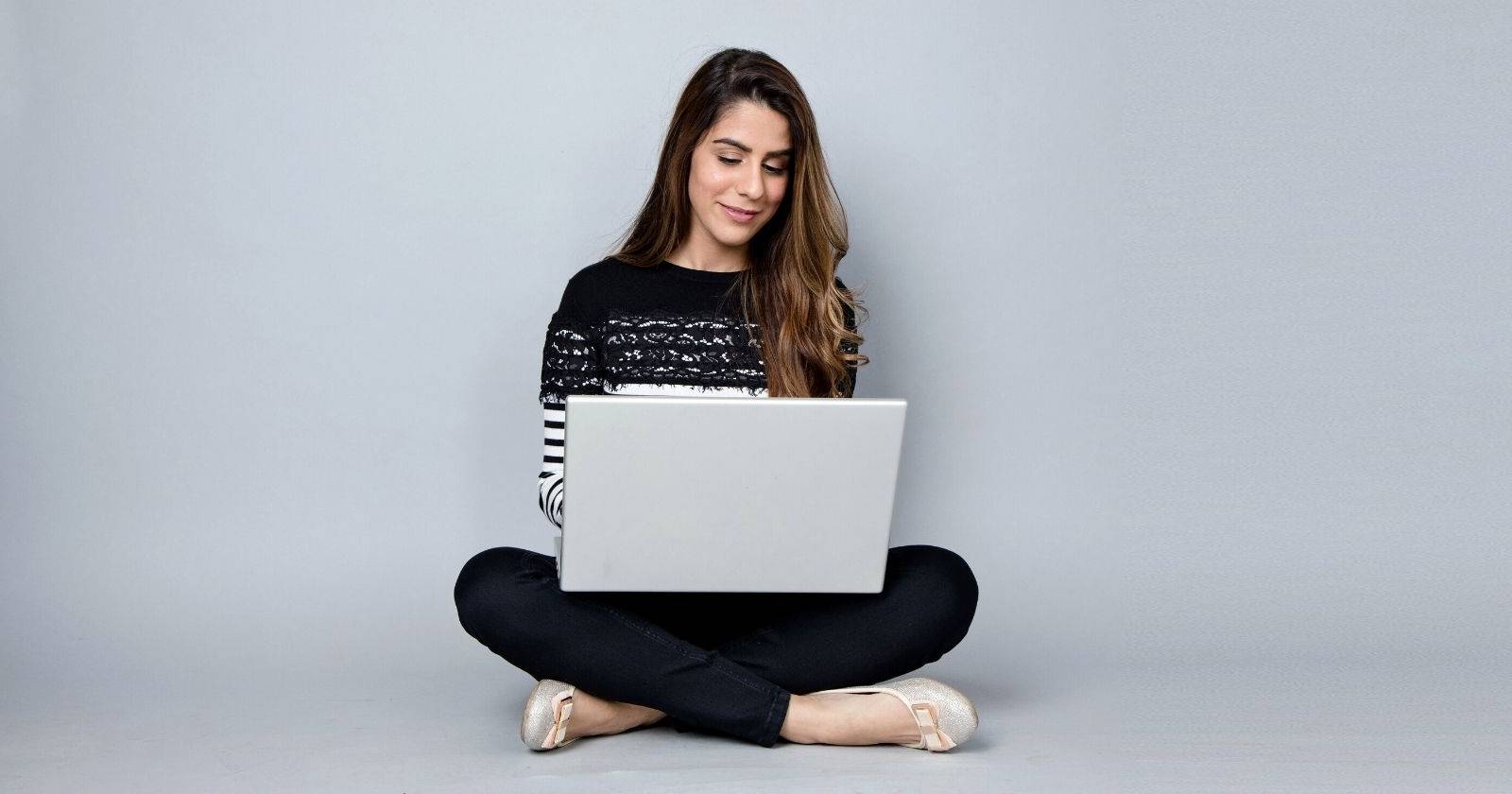 Девушка печатает на ноутбуке, опираясь о стену