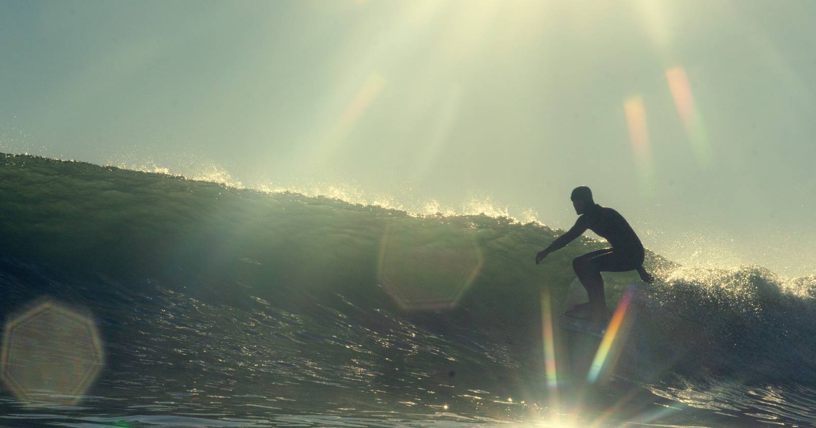 Сёрфер на волне с линзовым бликом и солнечными бликами на фото