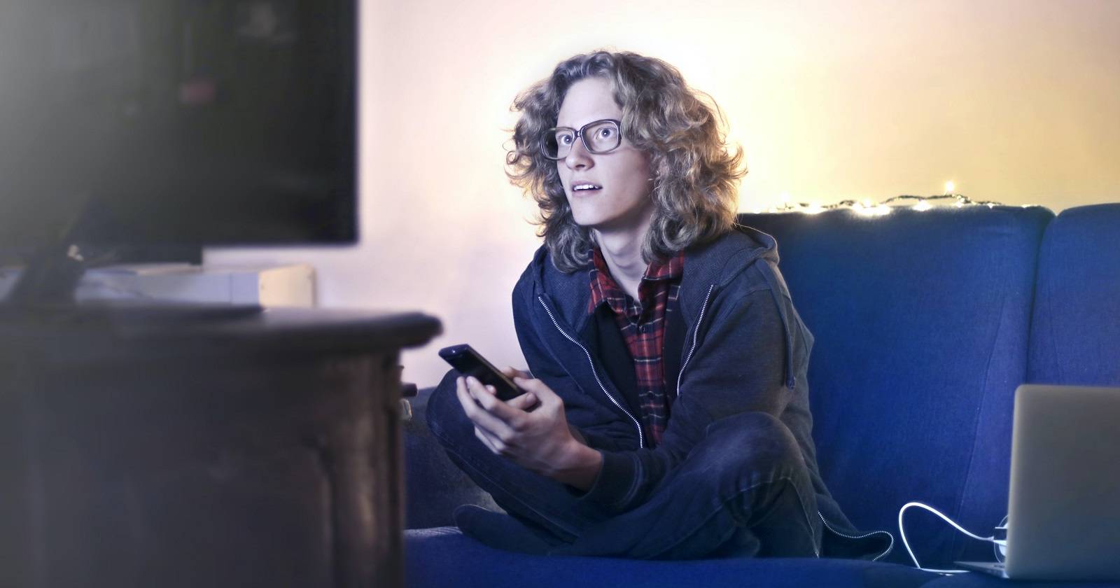 Человек смотрит телевизор с телефоном и ноутбуком рядом