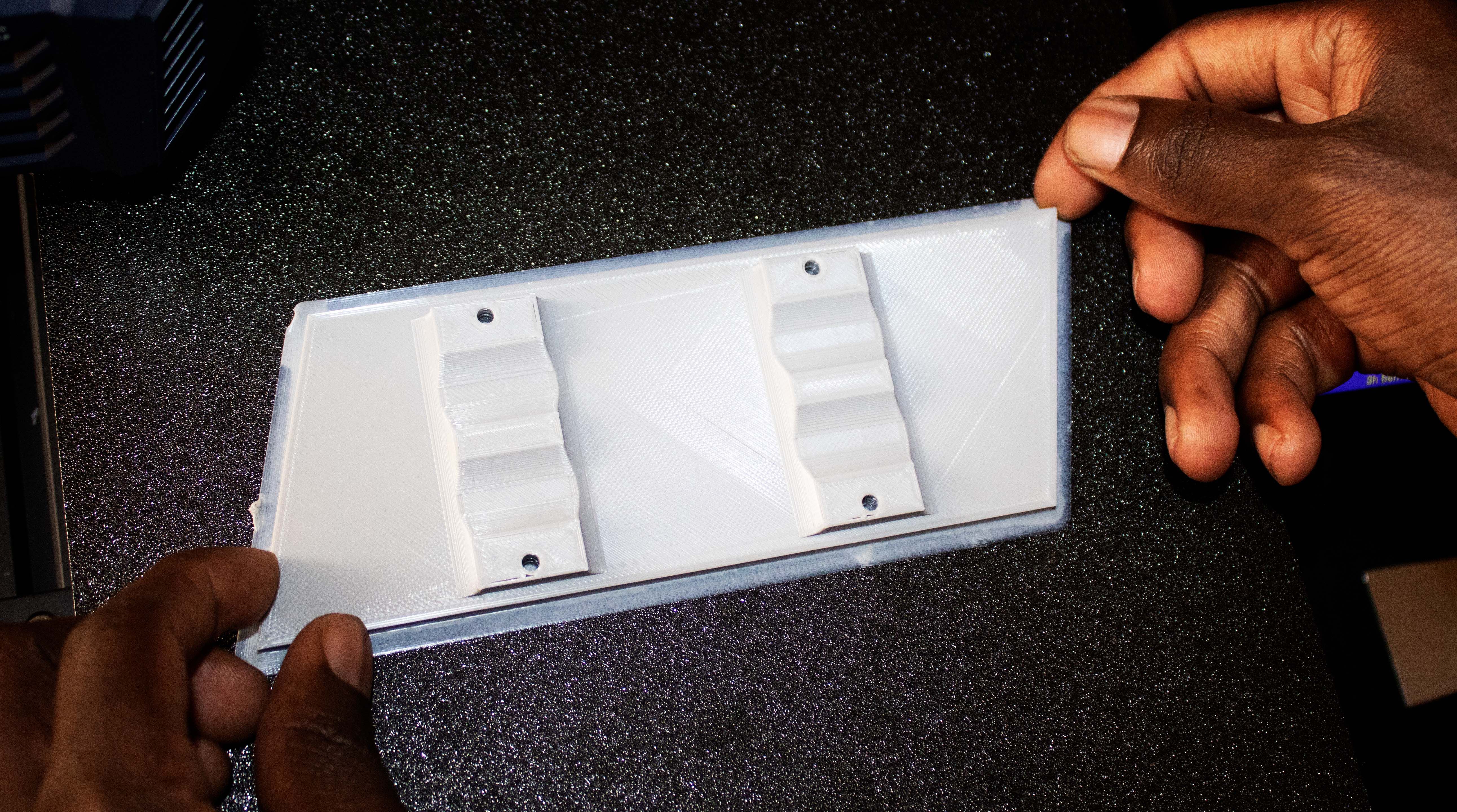 Две руки снимают белую 3D‑деталь со стола