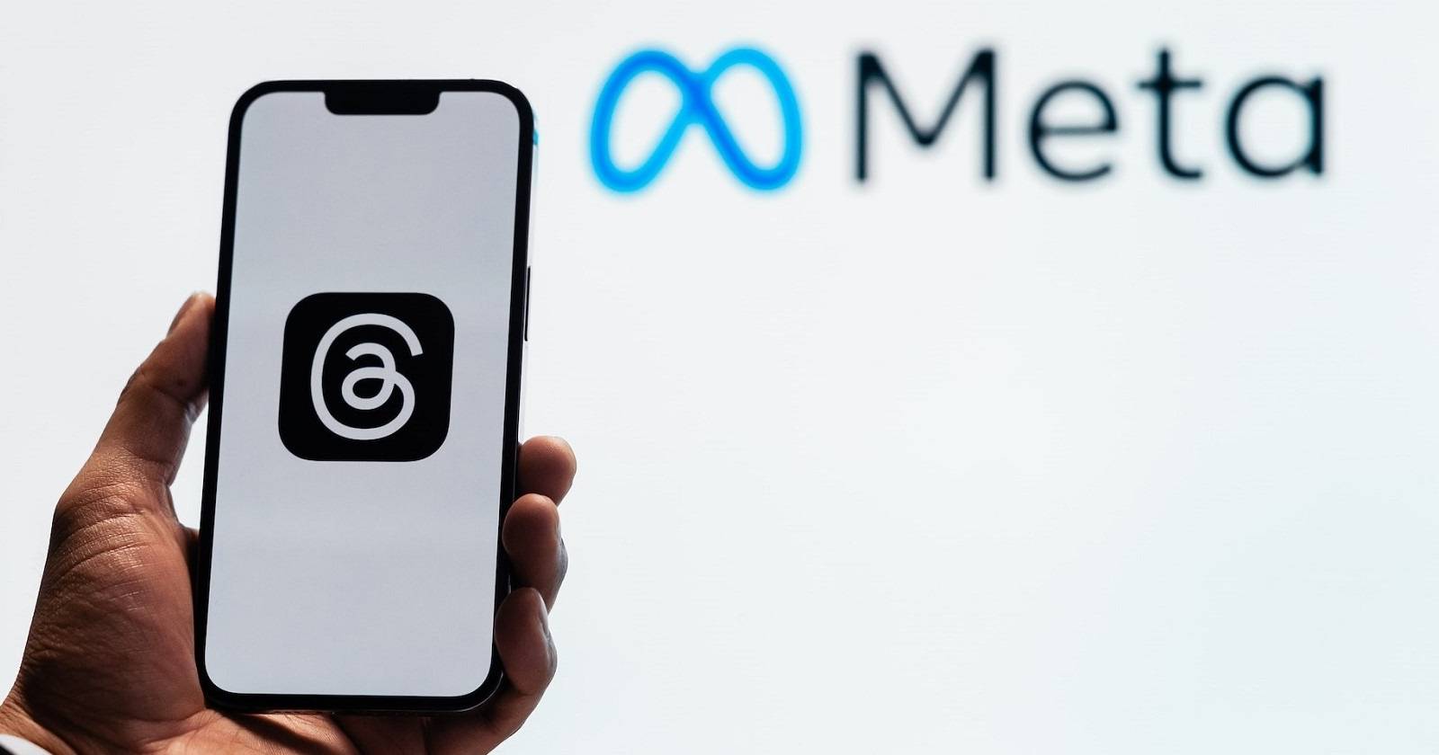 Рука держит смартфон с логотипом приложения Threads на фоне логотипа Meta