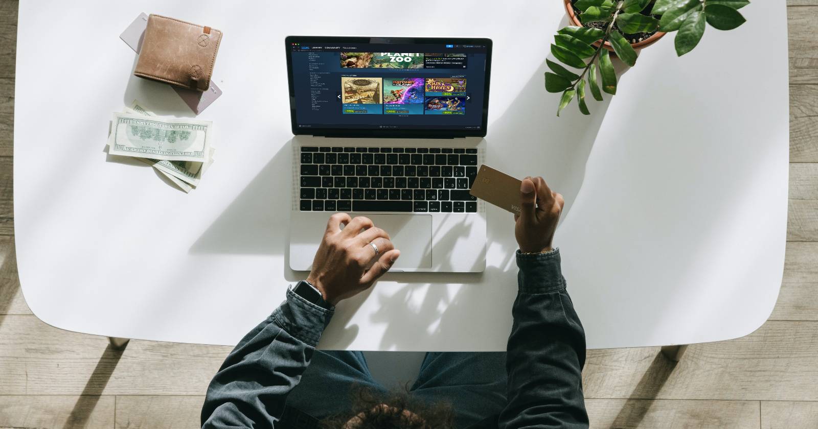 Мужчина держит банковскую карту и оплачивает покупку в Steam на MacBook