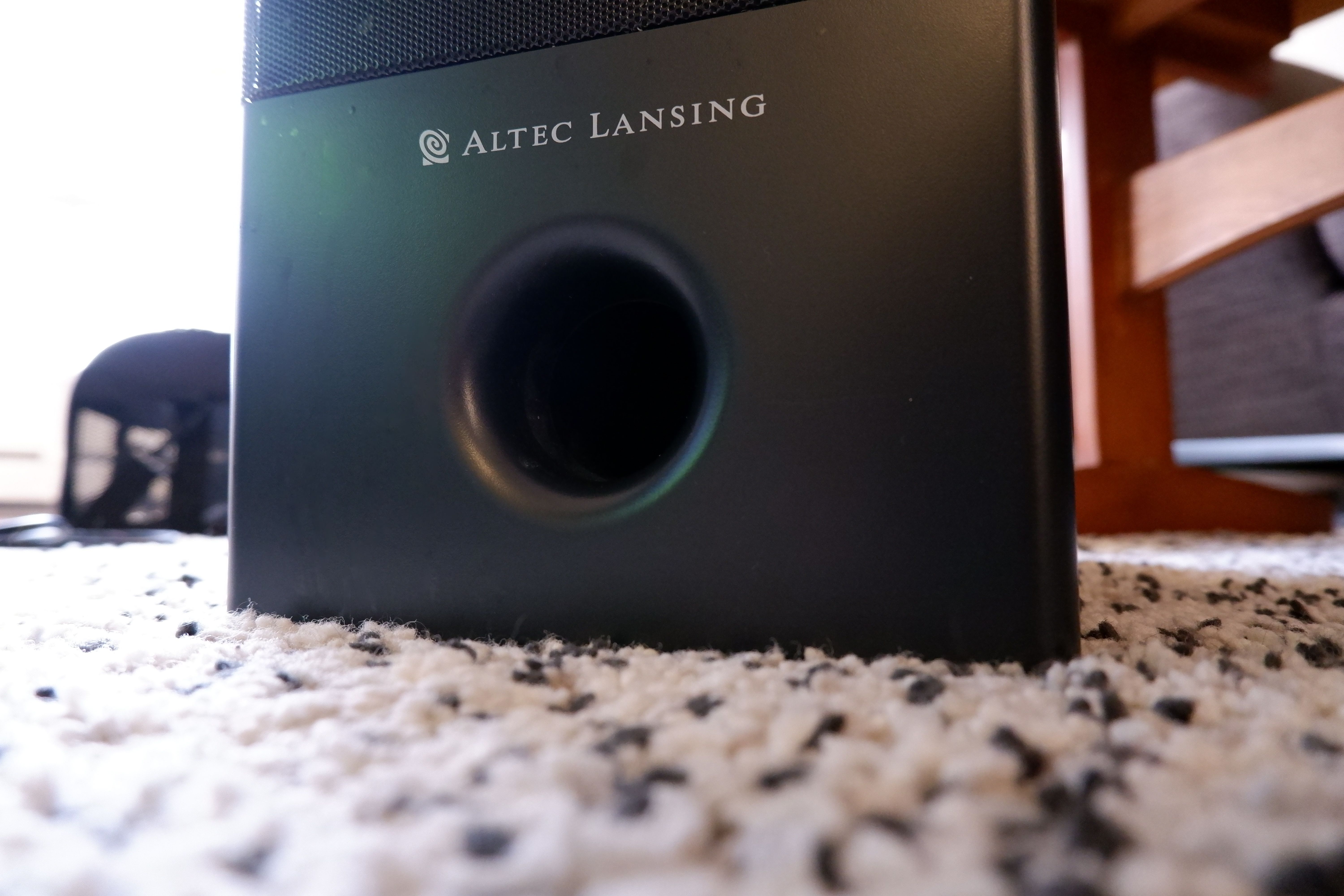 Сабвуфер на белом ковре с чёрными вкраплениями.