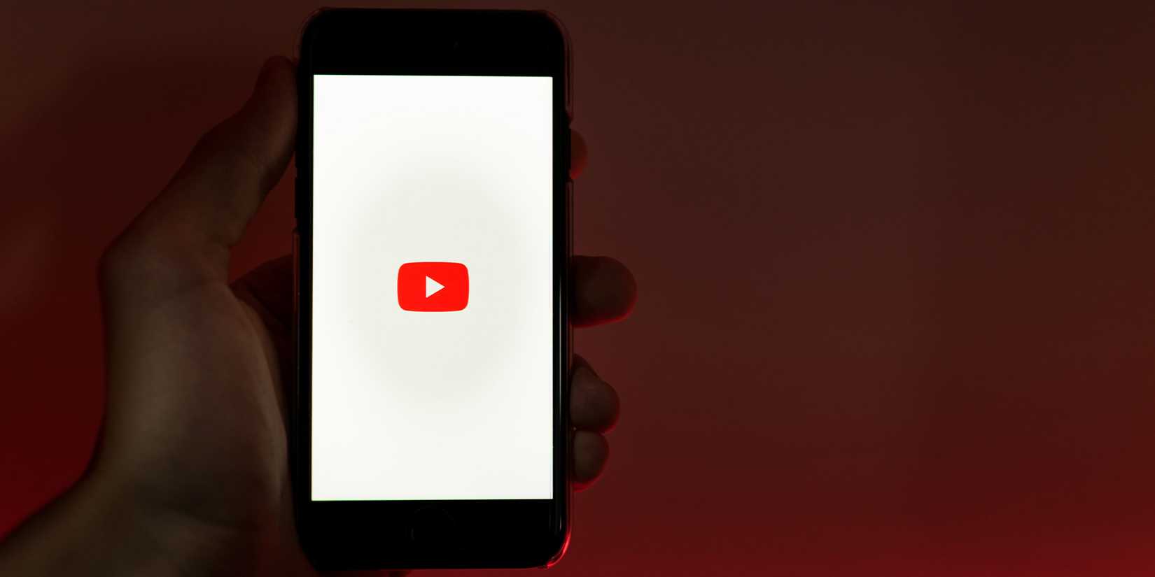 Человек держит смартфон с логотипом YouTube