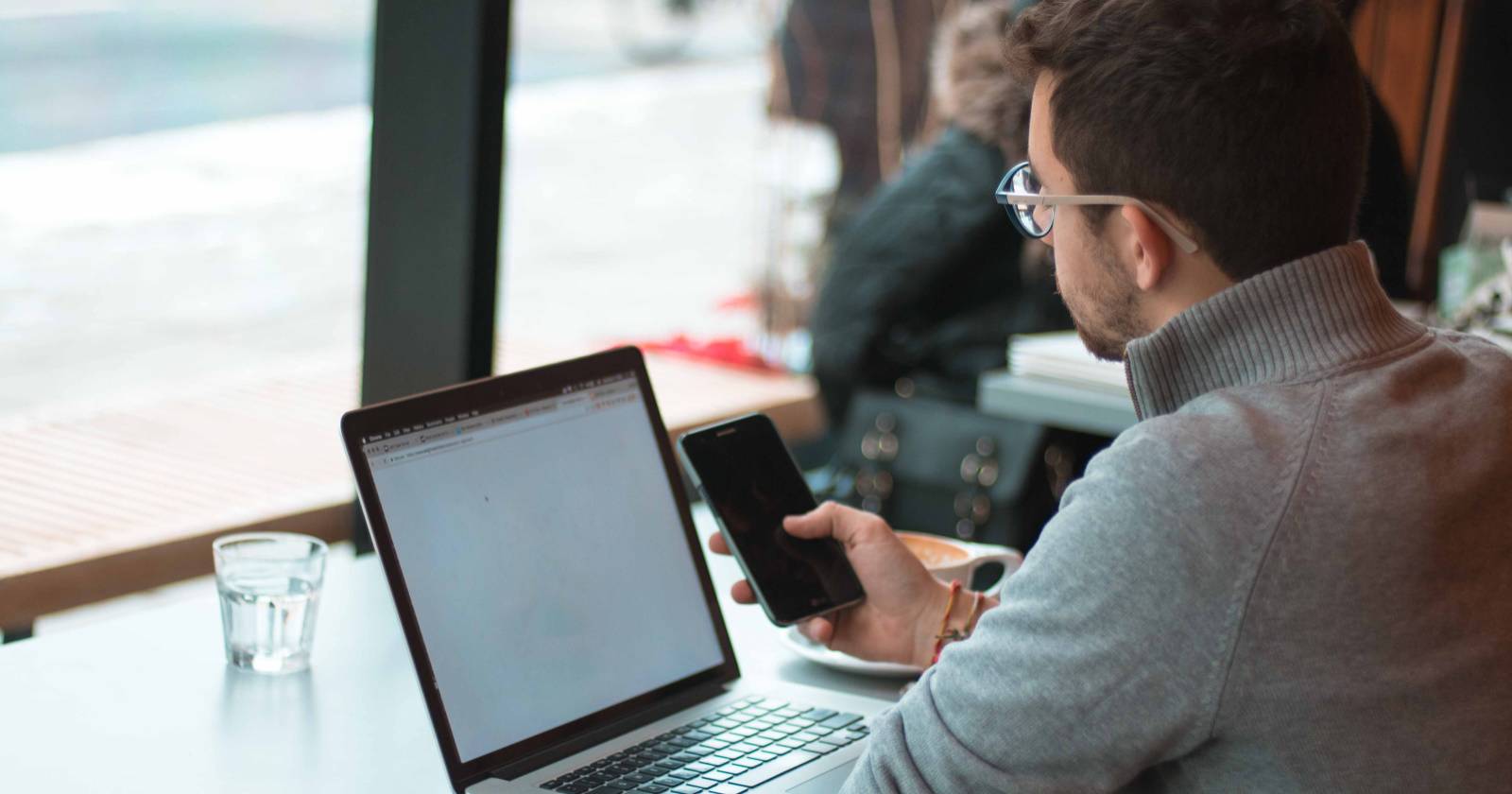 Мужчина работает за ноутбуком, держа мобильное устройство.