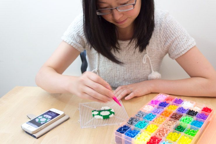 Рука с пинцетом выкладывает бусины на пегборд