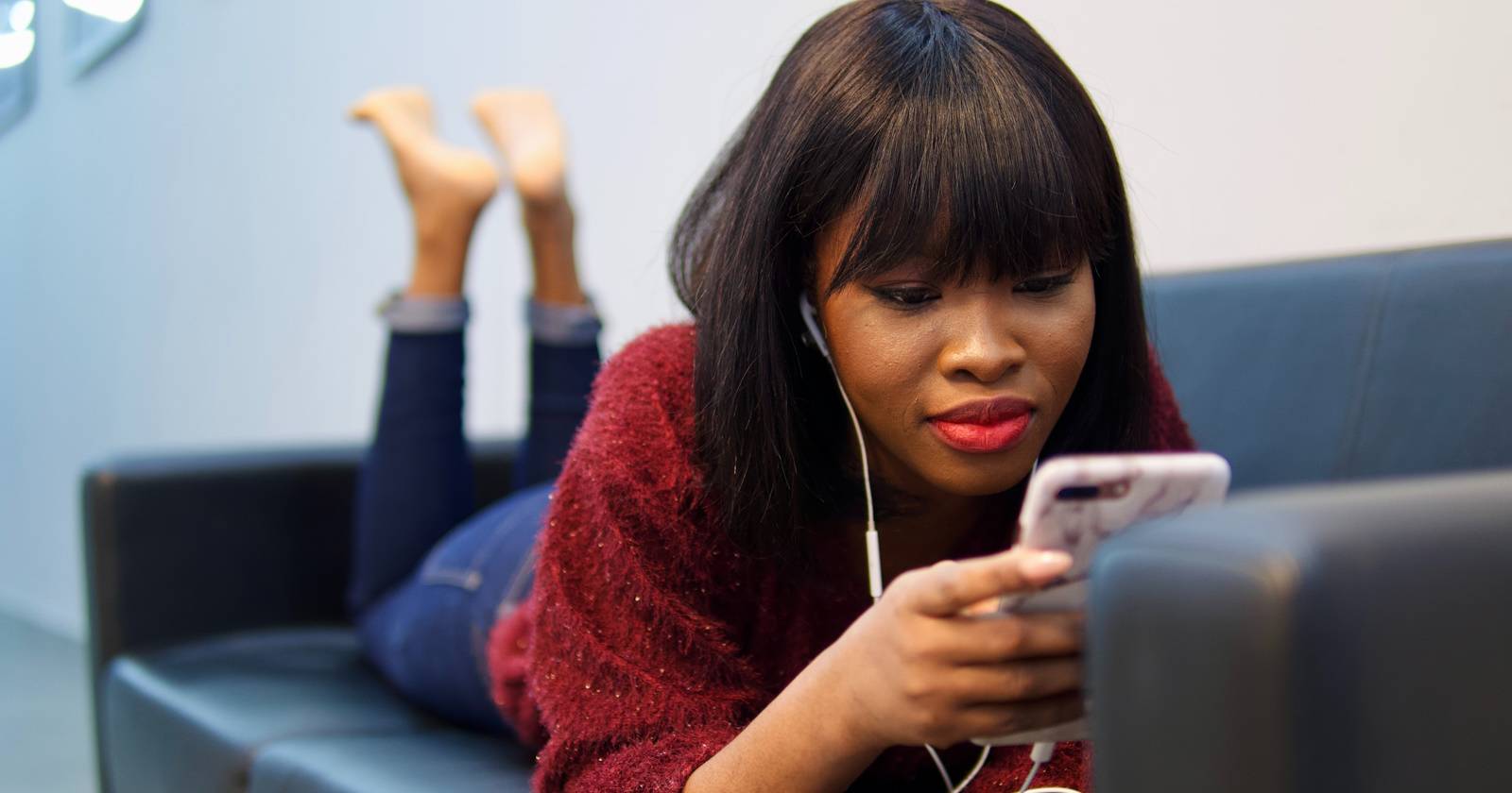 Женщина лежит на диване с наушниками и смартфоном