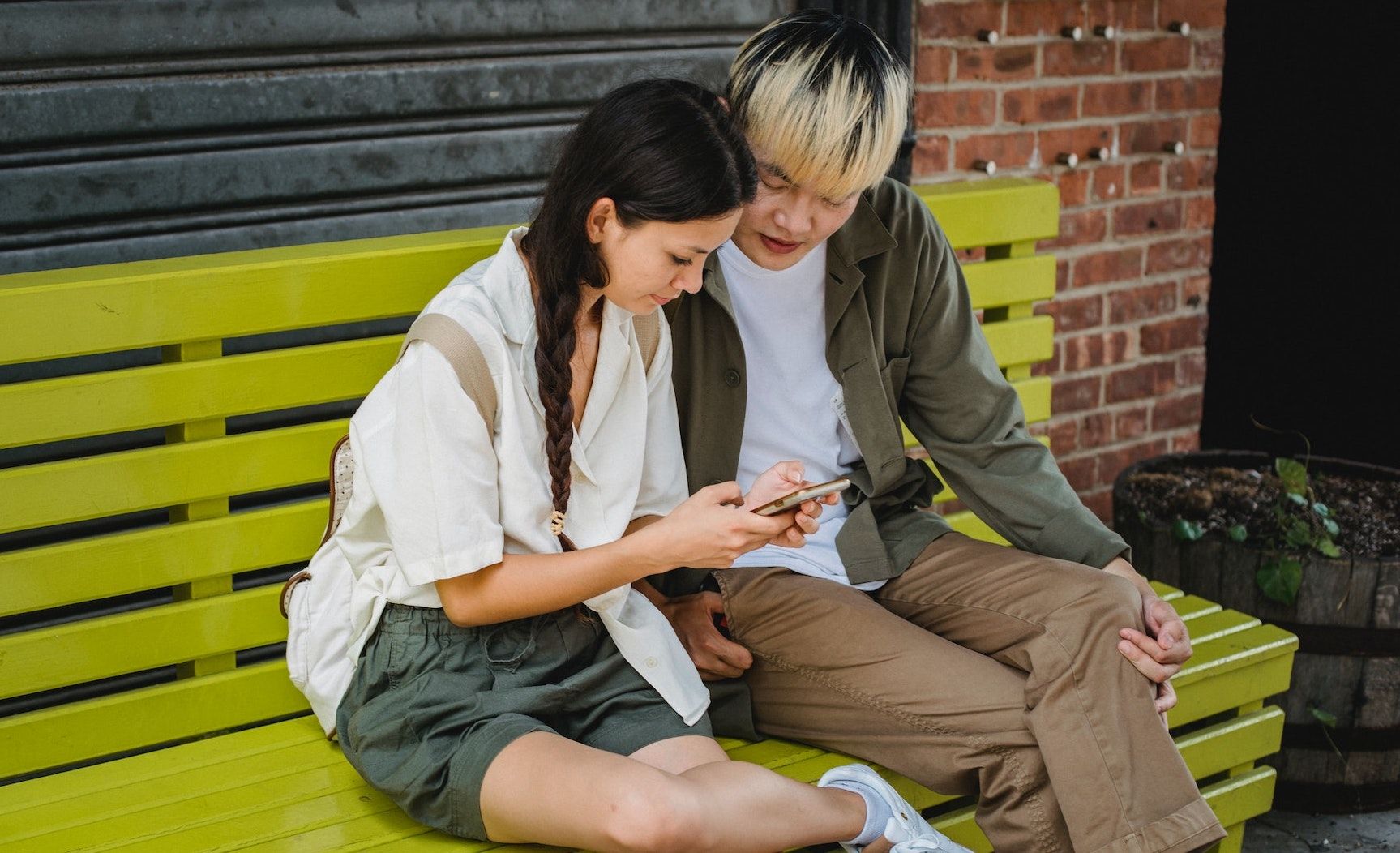 Мальчик и девочка сидят на улице и переписываются по смартфону
