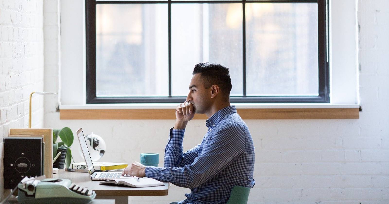 Мужчина работает за компьютером у окна