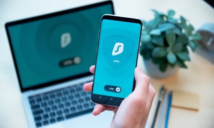человек держит телефон с показом VPN‑подключения над ноутбуком