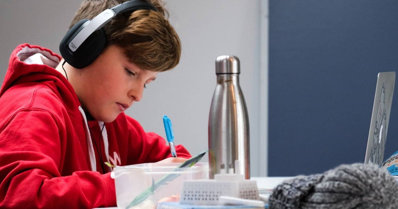 мальчик в красном худи и наушниках делает домашнее задание за ноутбуком