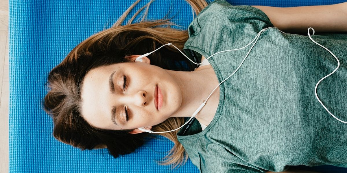 Спокойная женщина в наушниках отдыхает в позе шавасаны дома