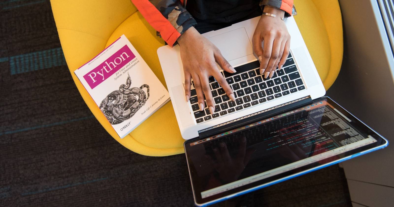 Человек программирует на ноутбуке, рядом лежит книга по Python
