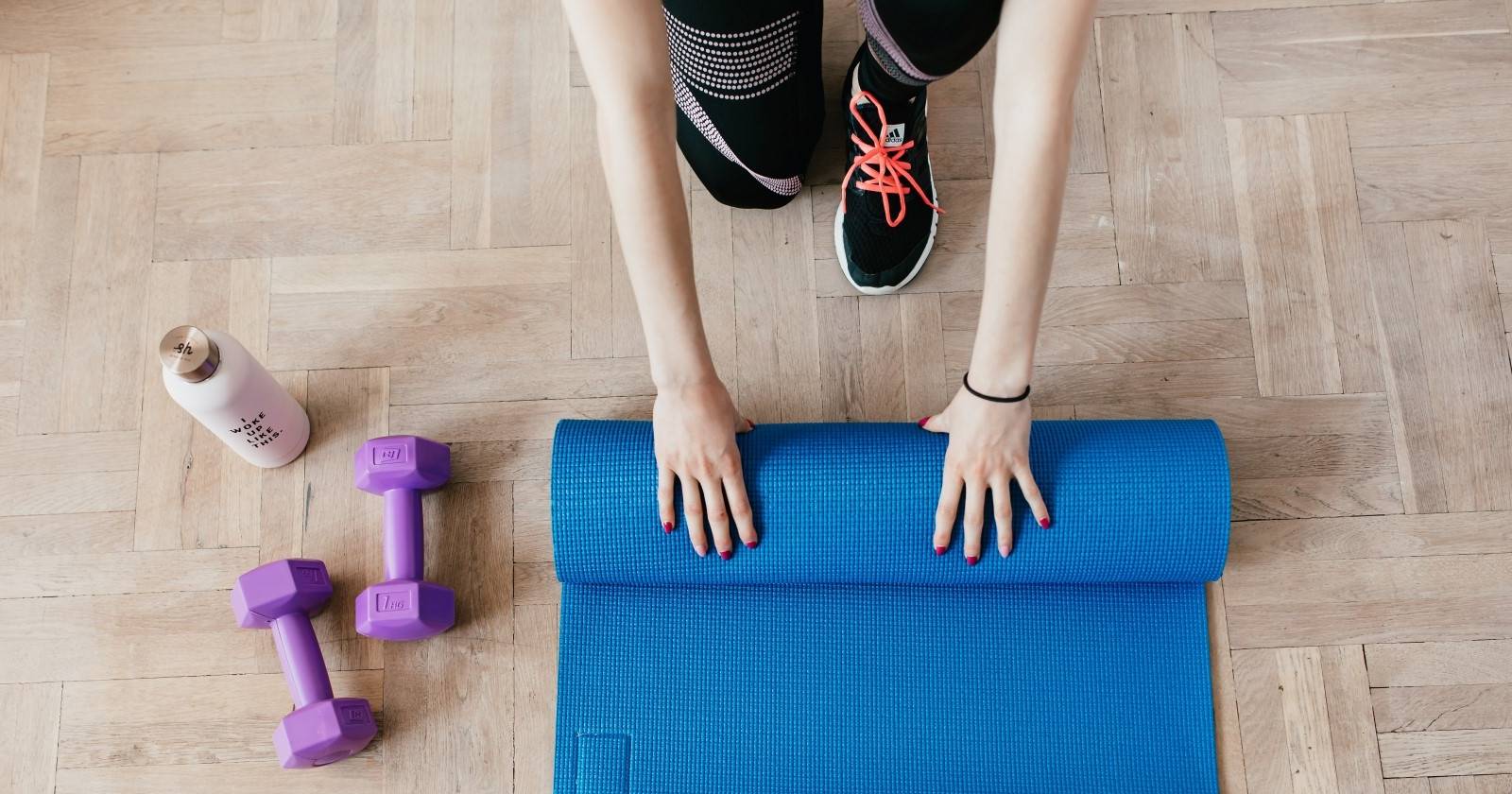 человек разматывает коврик для йоги рядом с гантелями