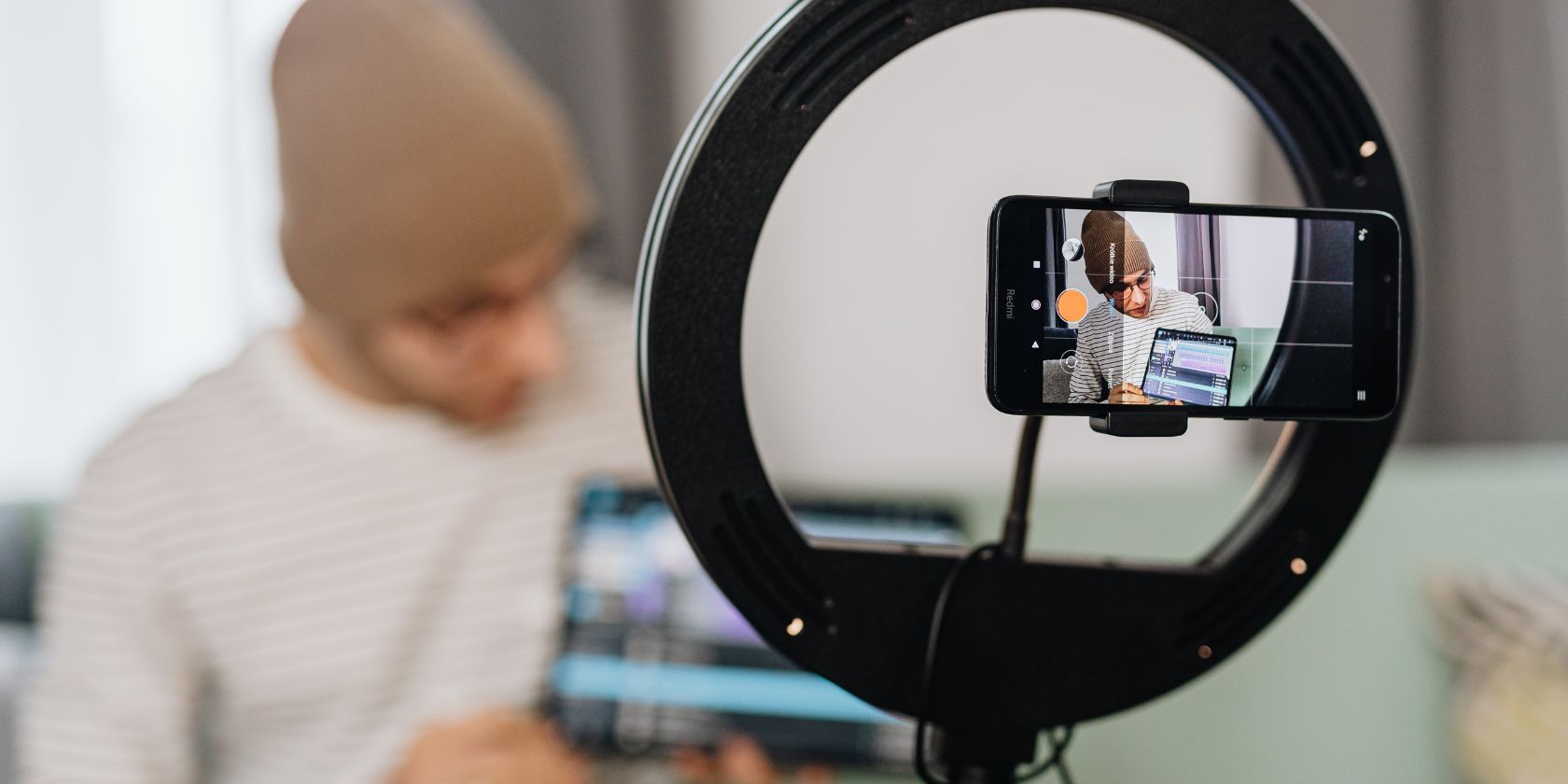 мужчина с бини и планшетом записывает влог с кольцевой лампой