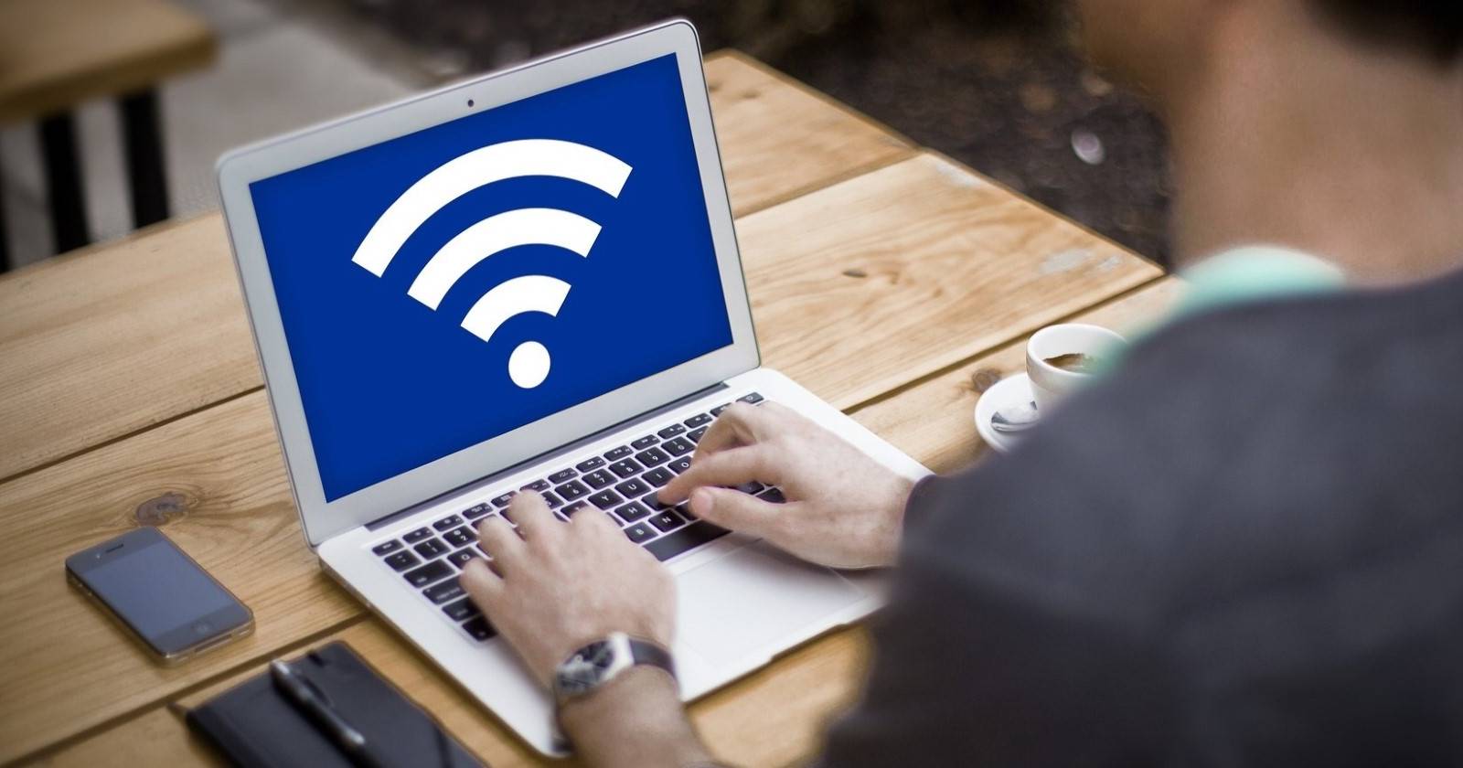 Мужчина за серебристым ноутбуком с иконкой Wi‑Fi на экране