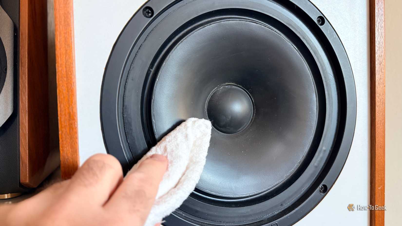 Человек аккуратно протирает низкочастотный динамик мягкой тряпкой.