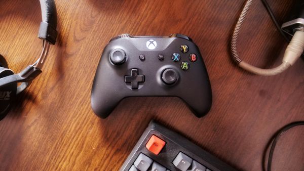 Геймпад Xbox One с гарнитурой и клавиатурой на деревянной поверхности.