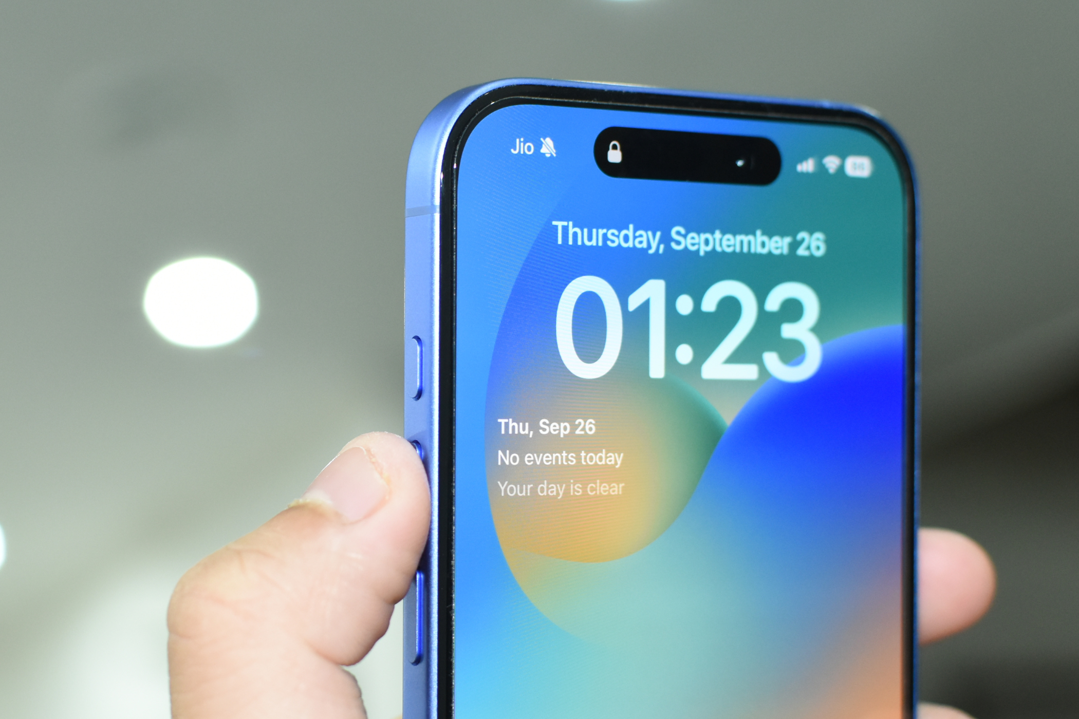 iPhone 16 в цвете Ultramarine, палец указывает на Action Button на левой грани.