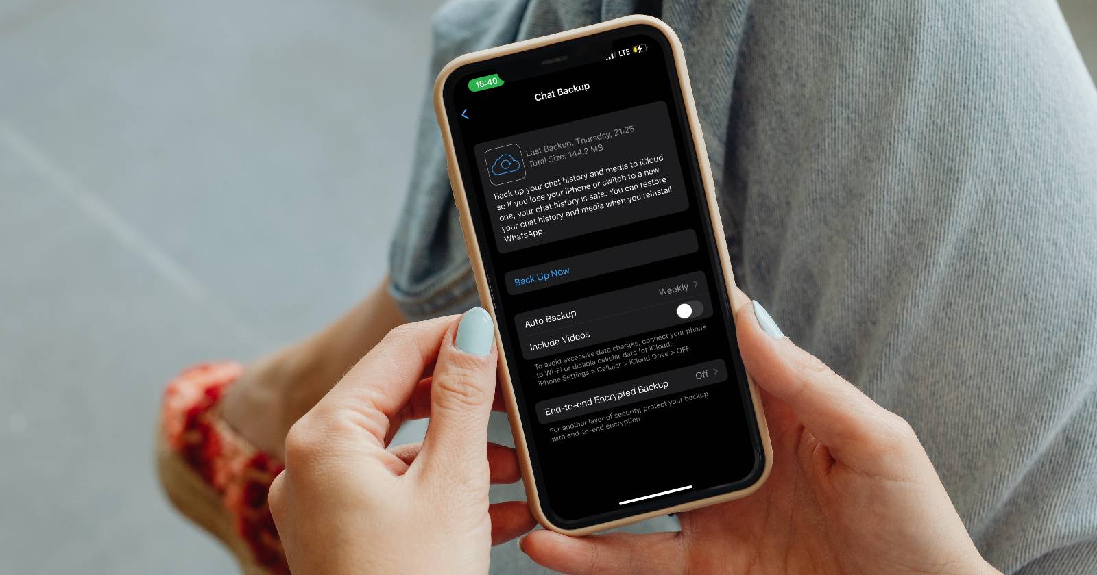 Женщина с разноцветными ногтями держит iPhone с экраном резервного копирования WhatsApp