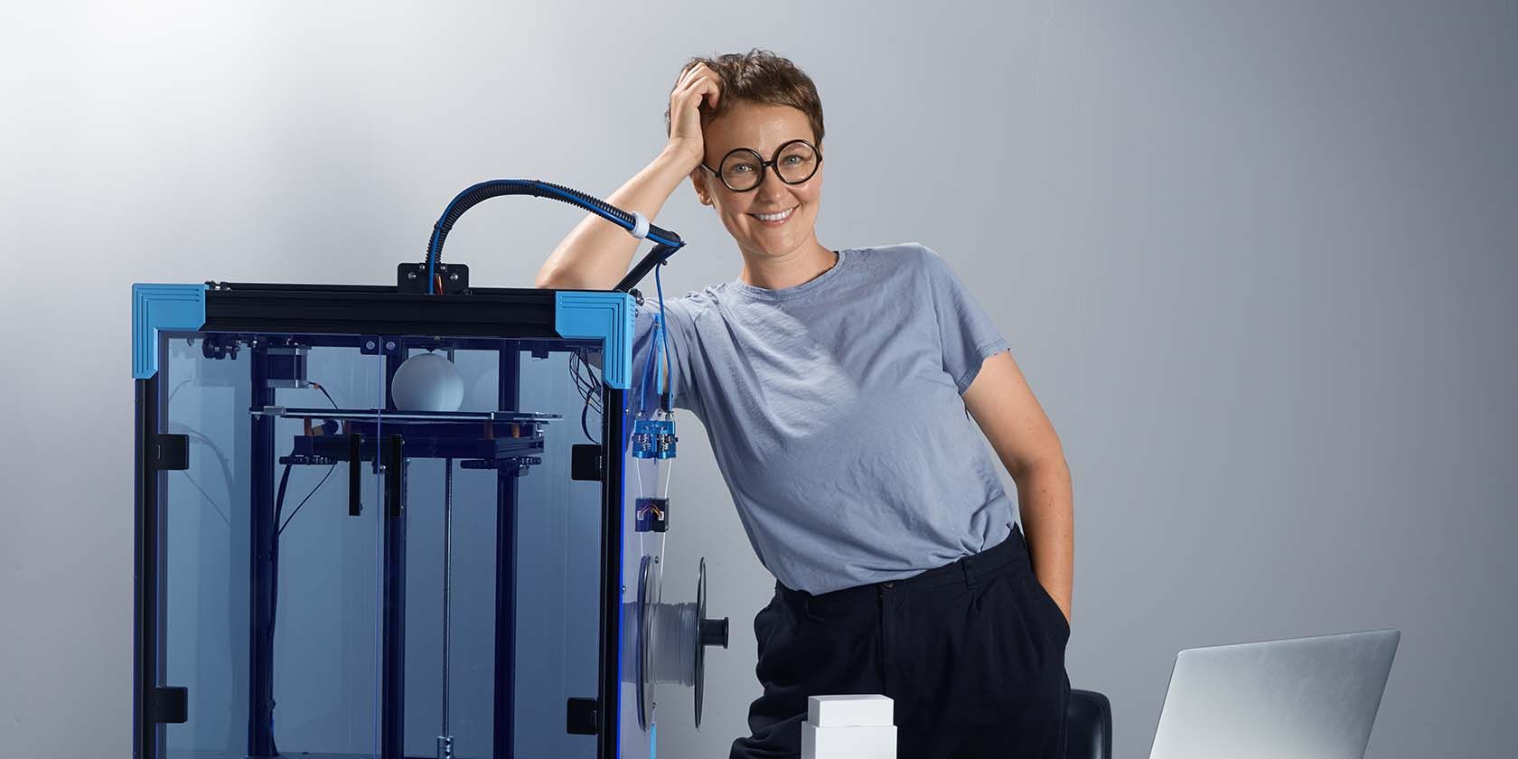Женщина стоит рядом с 3D‑принтером с улыбкой